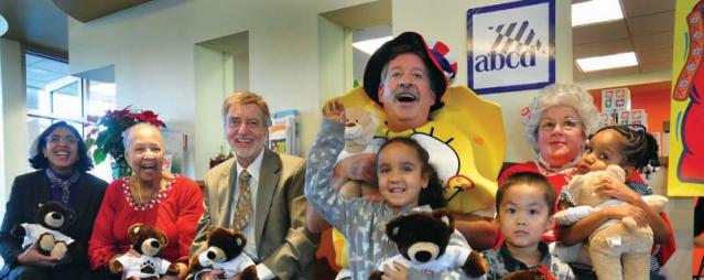 The ABCD Toy Drive received a welcome boost from partner Wainwright Bank at its Dorchester branch where children from the Gertrude Townsend Head Start Center on Geneva Avenue were treated to holiday festivities and given â€œBuild-A-Bearâ€ toys donated by accounting firm KPMG, a Toy Drive partner. Ken Jaffe, a bank VP, played Cookie Monster, Sponge Bob, and Hannah Montana while Mary Oâ€™Neill from Franklin was Mrs. Santa Claus. Joining in were, from left, Sharon Scott-Chandler, ABCD executive VP; Thelma Burns, ABCD Dorchester NSC board chair; John J. Drew, ABCD president/CEO; Jaffe; Oâ€™Neill, and happy Head Start children. 	  		  Photo by Don West